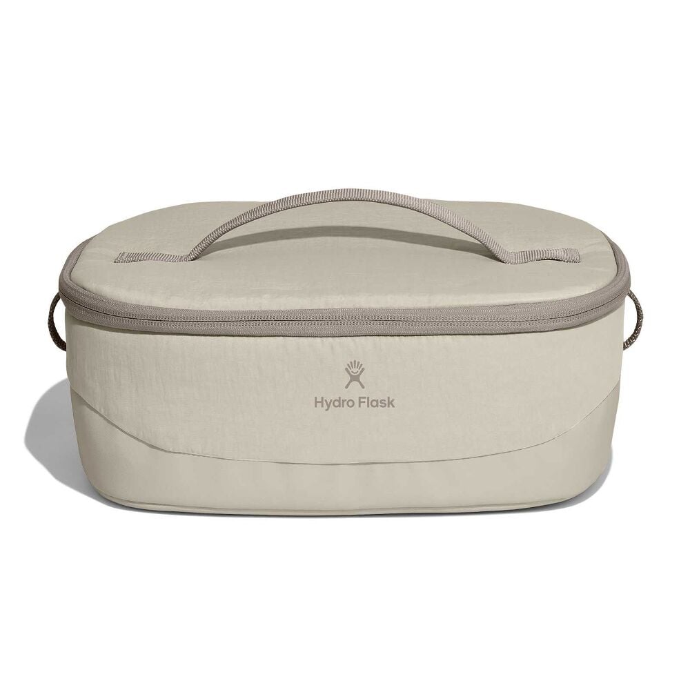 Beige Hydro Flask oval insulated bag with zip-around lid, fabric top handle, short side handles, and centered logo. Slightly structured base.